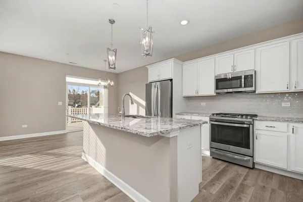 a kitchen with stainless steel appliances granite countertop a sink a stove a microwave a refrigerator and white cabinets