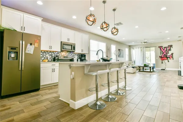 a kitchen with stainless steel appliances kitchen island granite countertop a stove a refrigerator a oven a sink a dining table and chairs with wooden floor