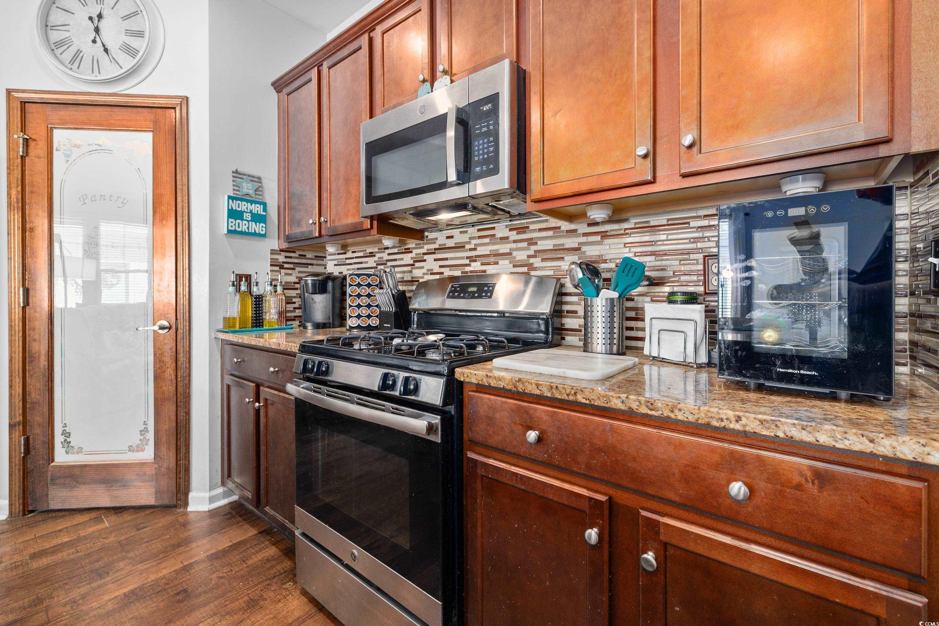 2360 Heritage Loop, Unit 2360 Myrtle Beach, SC 29577 - Photo 19 of 38 Kitchen with stainless steel appliances, tasteful backsplash, light stone counters, dark wood finished floors, and brown cabinets