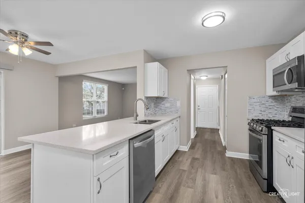a kitchen with a sink dishwasher a stove and white cabinets with wooden floor