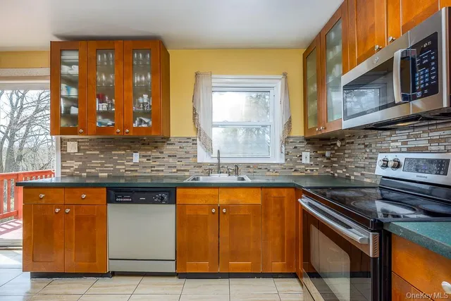 a kitchen with stainless steel appliances granite countertop wooden cabinets a stove a sink and a large window