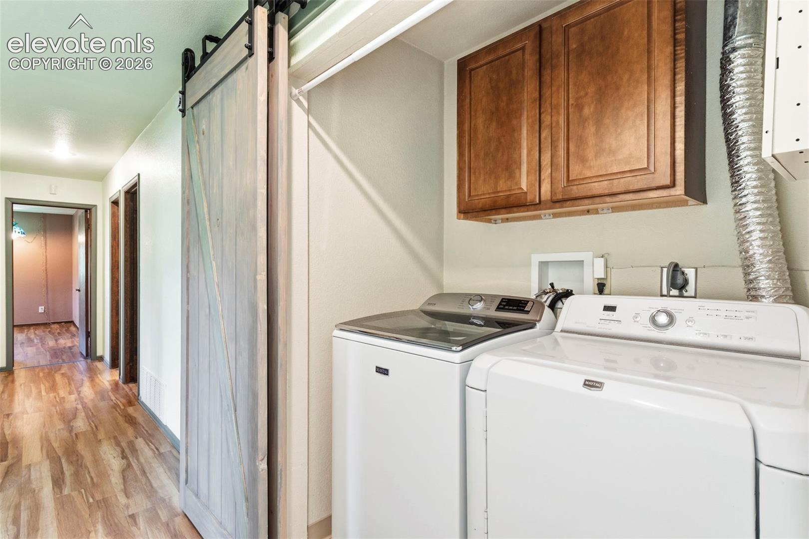 10765 Falling Star Road Fountain, CO 80817 - Photo 17 of 27 Laundry area featuring a sliding barn door, wood-finish flooring, and upper cabinetry