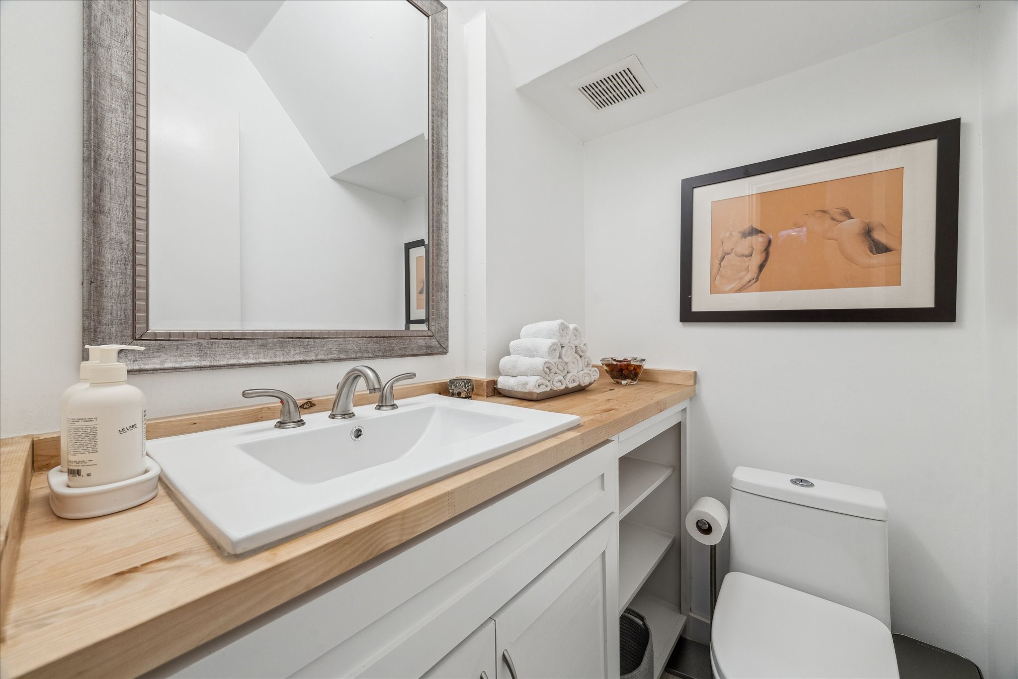 2100 Tanglewilde Street, Unit 373 Houston, TX 77063 - Photo 11 of 21 This downstairs powder room features a modern design with a sleek white sink and a natural custon wood countertop. The sink cabinet offers storage below with open shelves for towns books and artwork for display. A large mirror enhances and enlarges the space to complete a clean and inviting look.