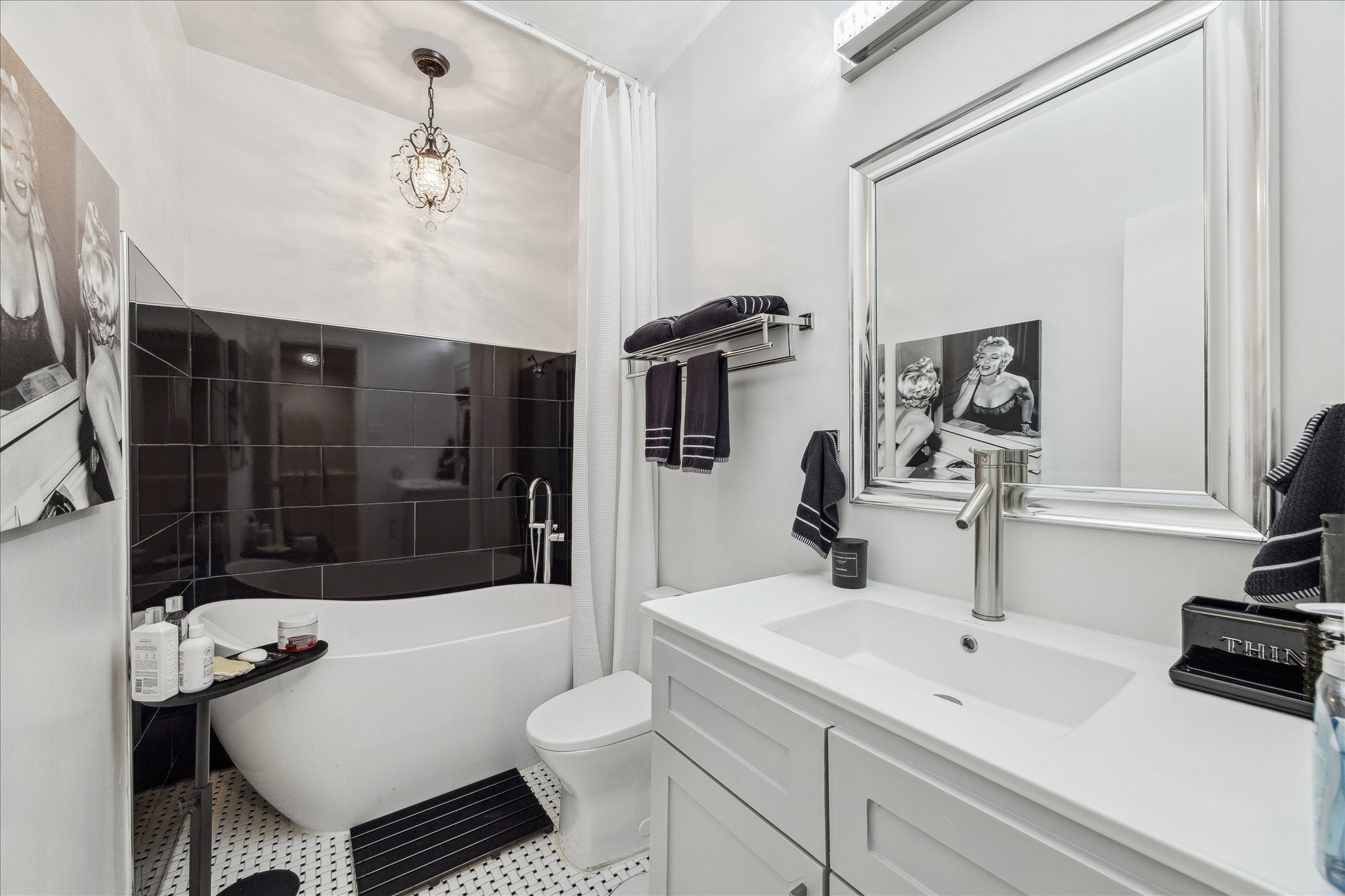 2100 Tanglewilde Street, Unit 373 Houston, TX 77063 - Photo 17 of 21 This stylish bathroom features a modern freestanding bathtub shower against a sleek black tile wall. It has elegant fixtures, a large mirrored vanity, and tasteful black-and-white decor, creating a chic and inviting space.