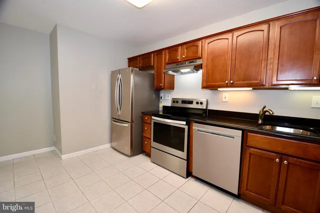 a kitchen with stainless steel appliances granite countertop a refrigerator a sink and dishwasher a stove with wooden cabinets