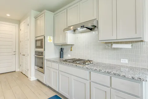 a kitchen with stainless steel appliances kitchen island granite countertop a stove a sink and white cabinets with wooden floor