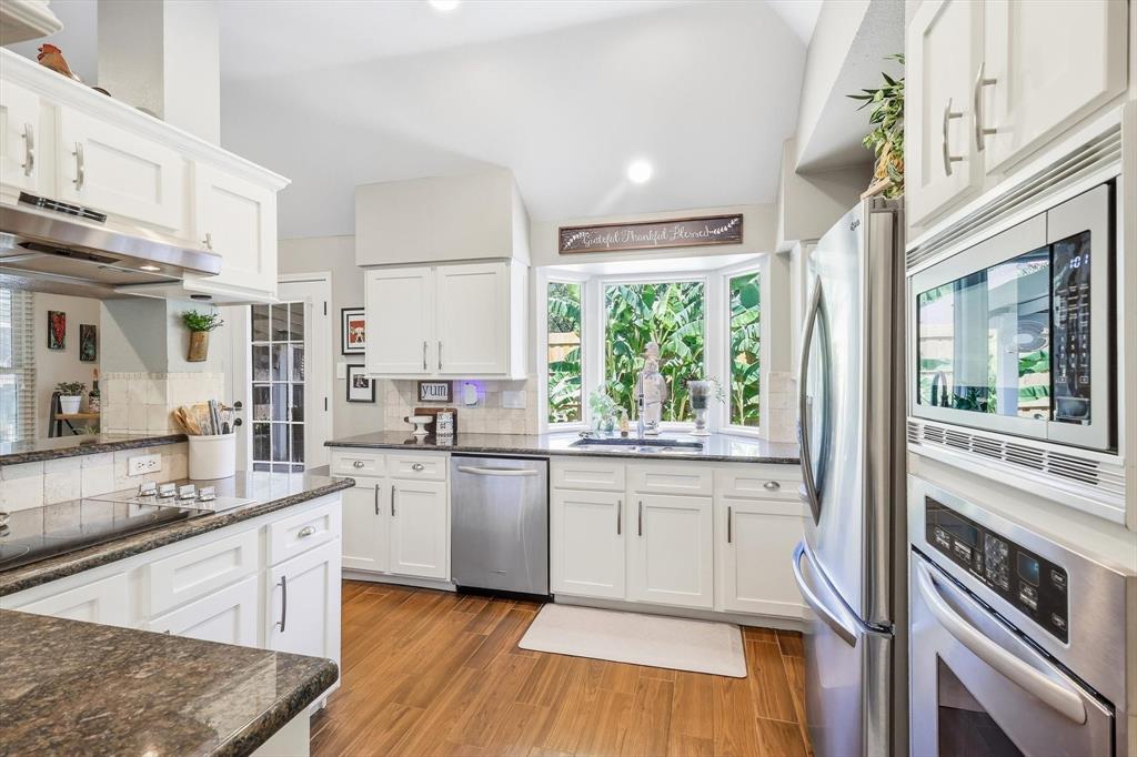 524 Post Oak Road Grapevine, TX 76051 - Photo 12 of 37 White cabinetry, stainless steel appliances, wood-finish flooring, vaulted ceiling, and a bay window