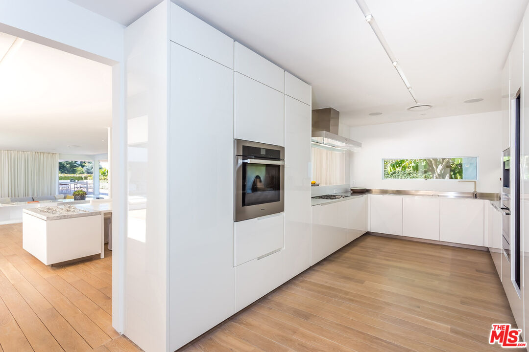 1106 North Hillcrest Road Beverly Hills, CA 90210 - Photo 22 of 54 a view of a kitchen and an empty room with wooden floor