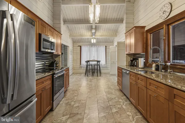 a large kitchen with stainless steel appliances granite countertop a stove top oven a sink dishwasher a dining table and chairs with wooden floor
