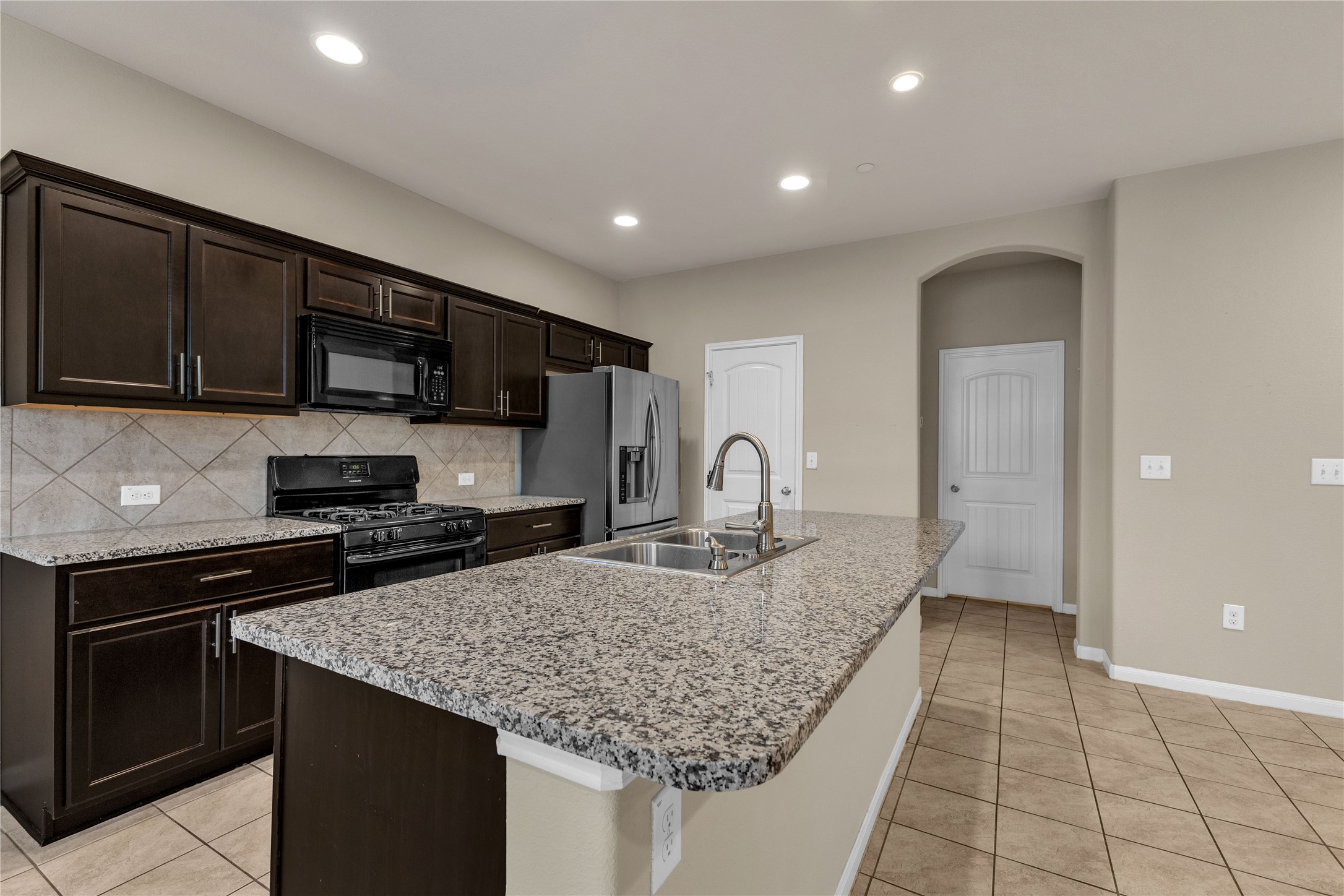2880 Donnell Drive, Unit 2003 Round Rock, TX 78664 - Photo 13 of 31 Kitchen featuring an expansive island with a stainless steel sink and gooseneck faucet, dark wood cabinetry, granite countertops, tile backsplash, and recessed lighting