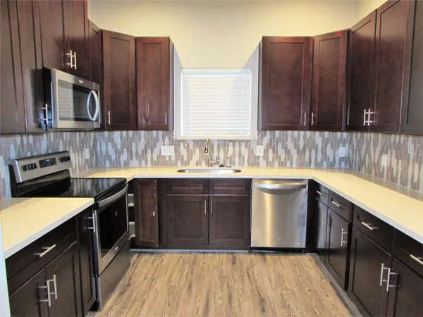 a kitchen with a sink dishwasher a stove top oven a refrigerator with wooden cabinets and floor