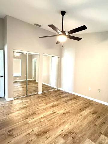 a view of an empty room with wooden floor and a ceiling fan