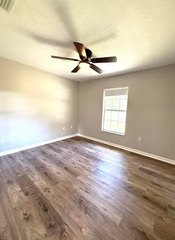 an empty room with wooden floor ceiling fan and windows