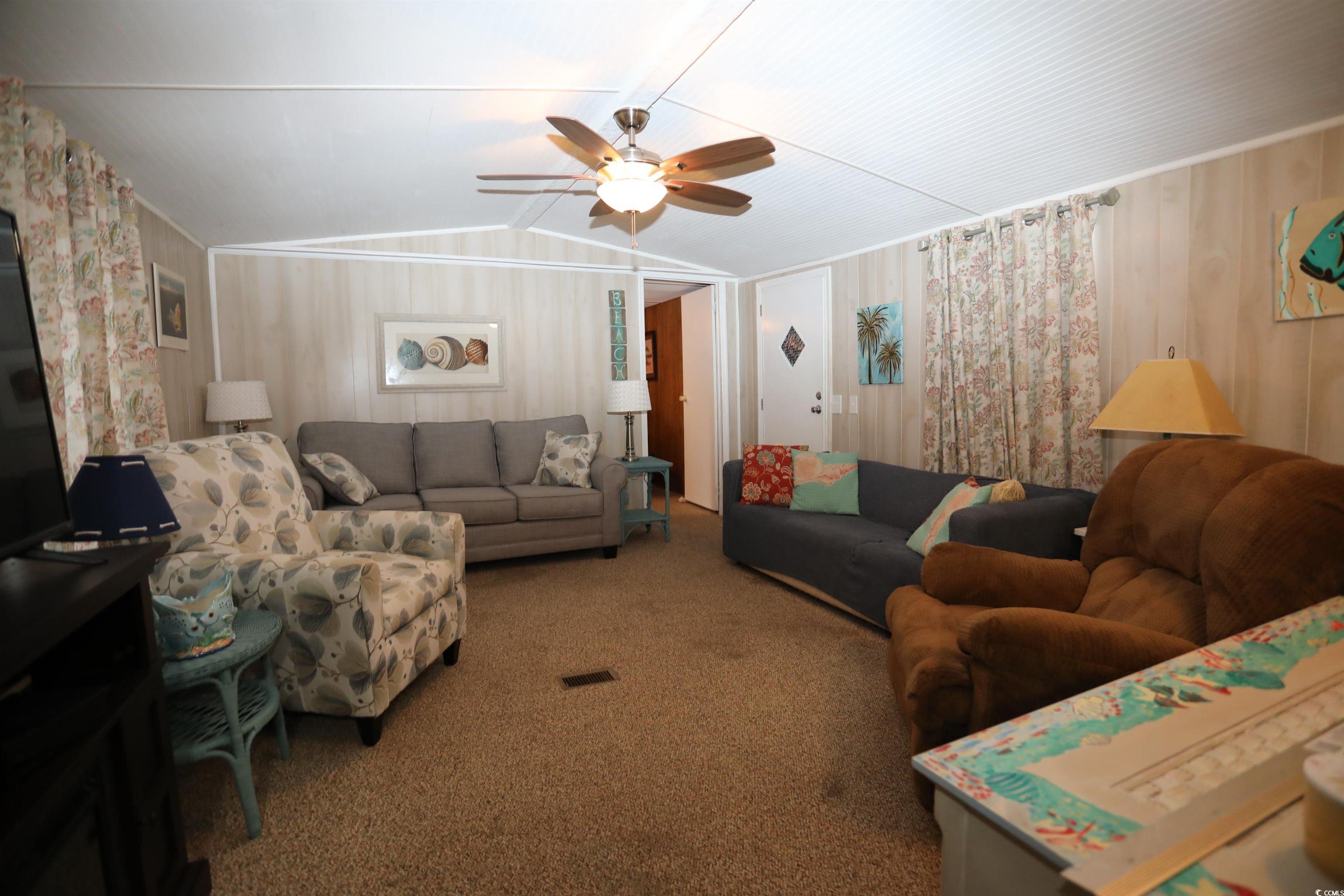 724 1st Street Murrells Inlet, SC 29576 - Photo 17 of 18 Carpeted living area with vaulted ceiling, ceiling fan, and wood walls