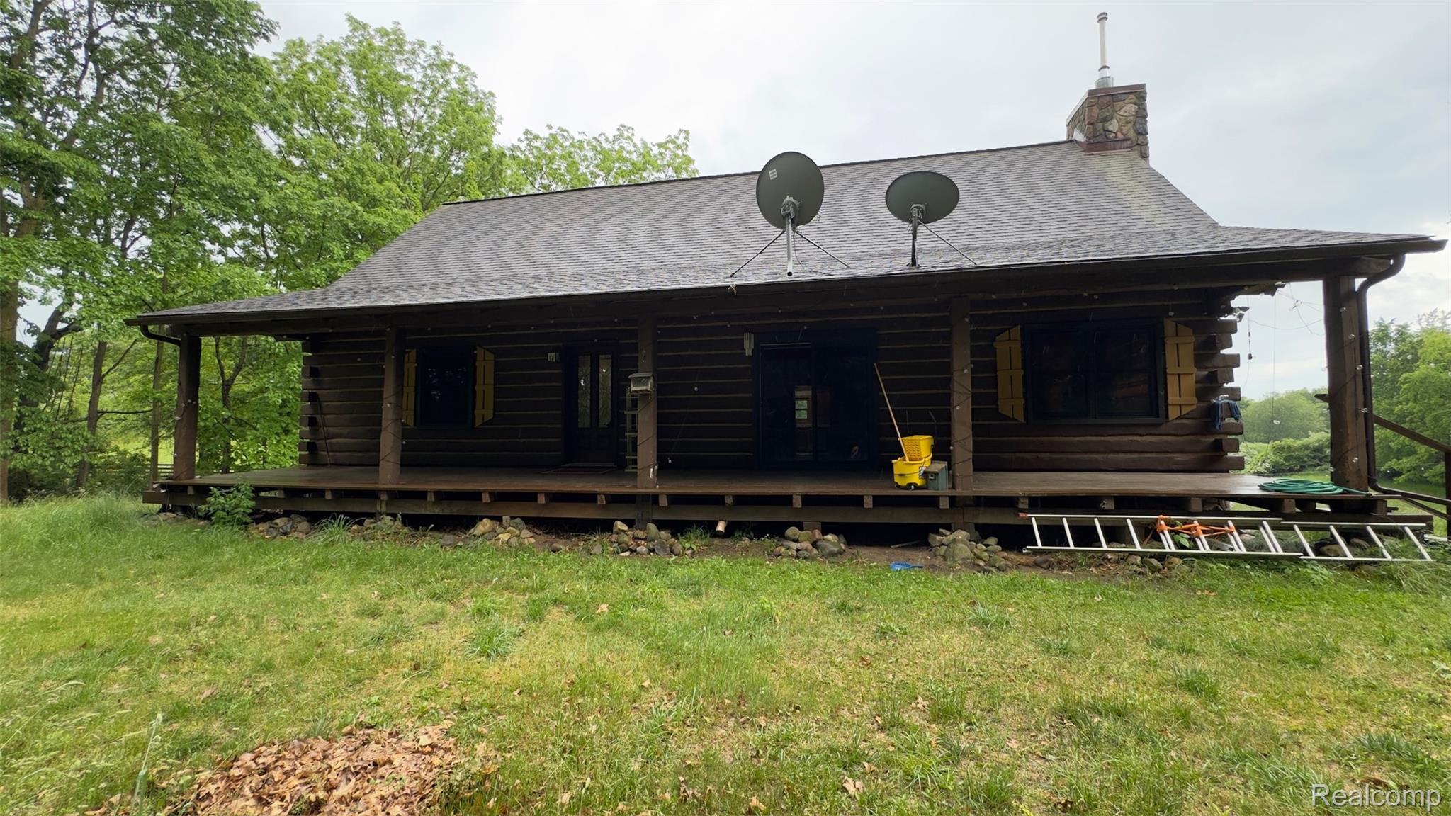 2608 East Sutton Road Metamora, MI 48455 - Photo 42 of 64 Rustic log cabin exterior featuring a covered porch, stone chimney, wood-finish siding, and a dark shingle roof