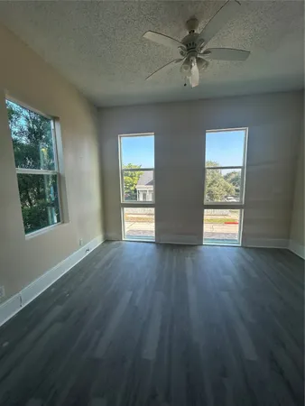 an empty room with wooden floor chandelier fan and windows