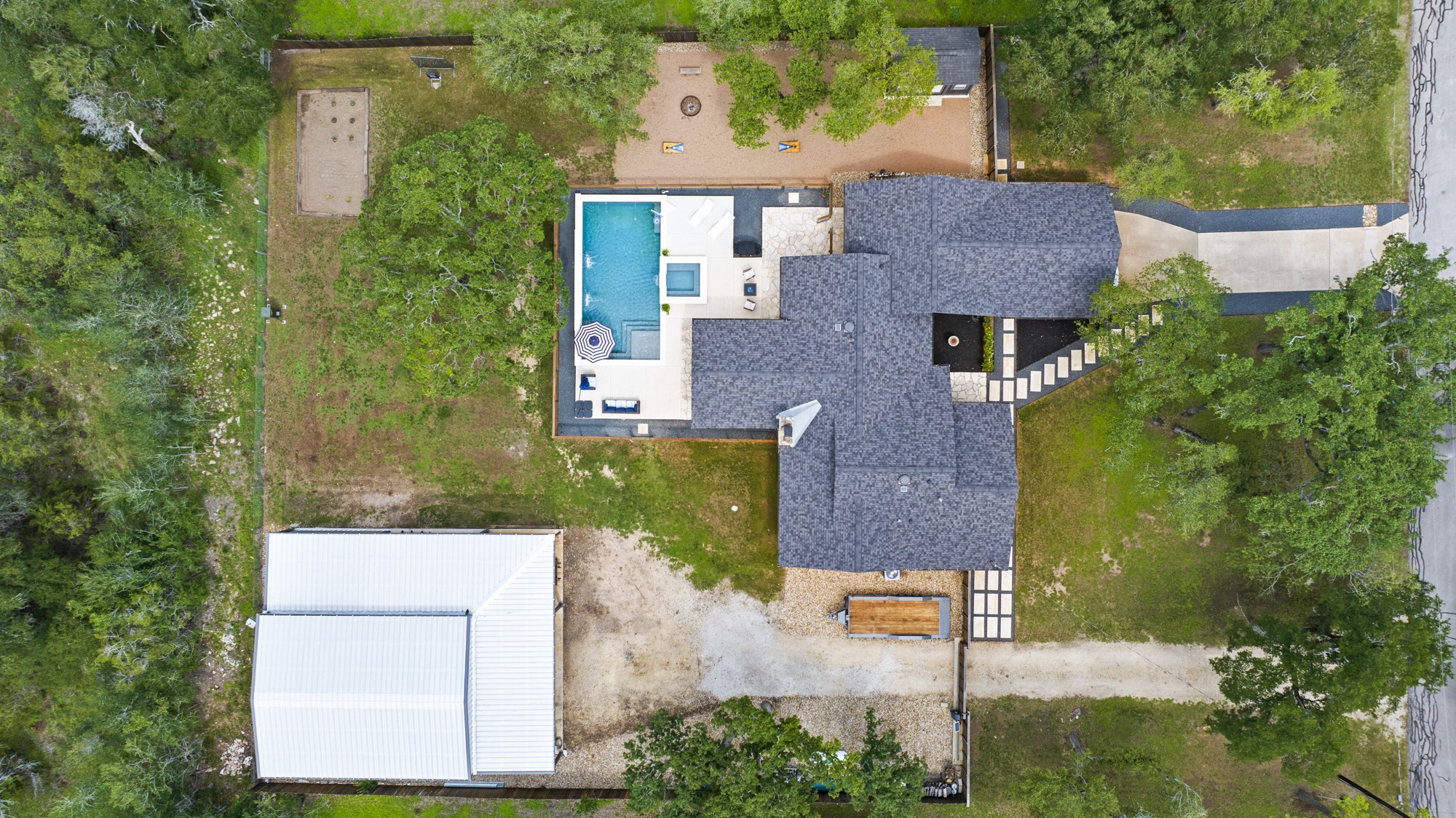 2802 Robin Road Manchaca, TX 78652 - Photo 4 of 40 Expansive property featuring a central residence with a shingle roof, a rectangular swimming pool with an integrated spa, and an additional outbuilding with a metal roof