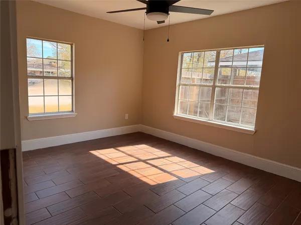 an empty room with wooden floor fan and windows
