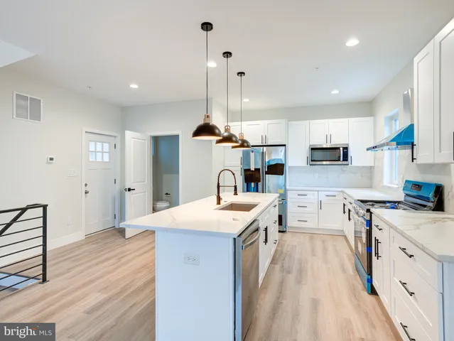 a large kitchen with stainless steel appliances granite countertop a stove a sink dishwasher a refrigerator white cabinets and wooden floor