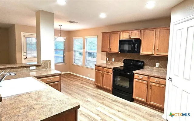 a kitchen with stainless steel appliances granite countertop a stove top oven a sink dishwasher a refrigerator and a dining table with wooden floor