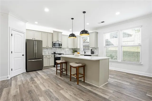 a kitchen with stainless steel appliances granite countertop a refrigerator a sink dishwasher a stove and white cabinets with wooden floor