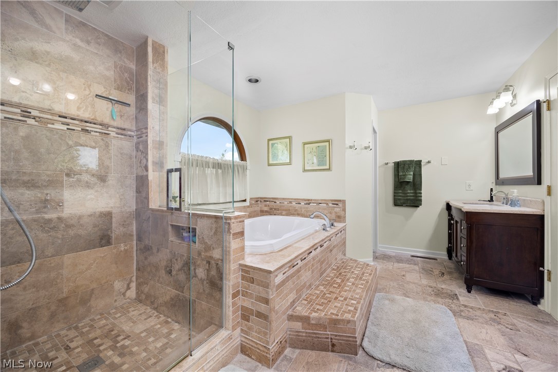 3270 North Ridge Road Vermilion, OH 44089 - Photo 31 of 49 Walk-in shower with glass enclosure, separate soaking tub with tiled surround, arched window, and a single vanity with stone-finish countertop