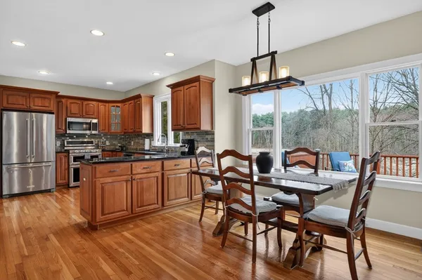 a kitchen with stainless steel appliances granite countertop a stove a refrigerator a microwave a dining table and chairs with wooden floor