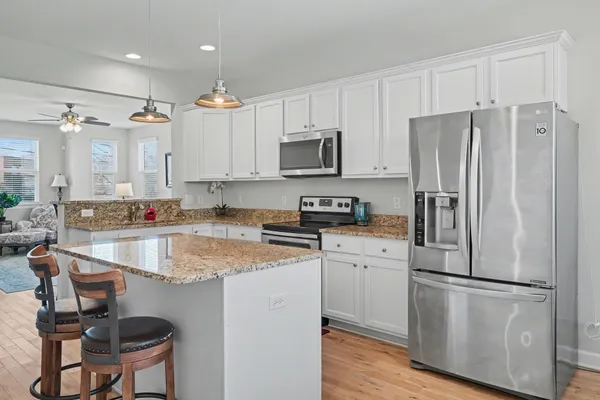 a kitchen with granite countertop a refrigerator a stove a sink dishwasher and white cabinets with wooden floor