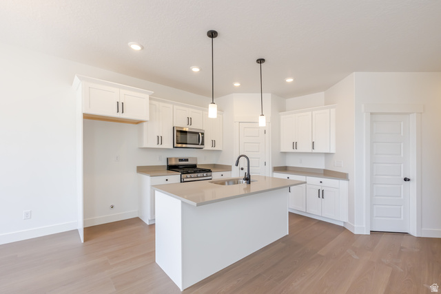 5224 South Acacia Drive, Unit 809 Mapleton, UT 84664 - Photo 7 of 23 Modern kitchen featuring light wood-finish flooring, white cabinetry with dark hardware, a central island with an undermount sink, pendant lighting, and stainless steel appliances