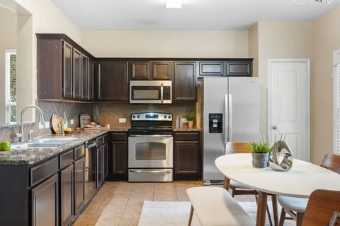 a kitchen with stainless steel appliances granite countertop a refrigerator a stove a sink a dining table and chairs