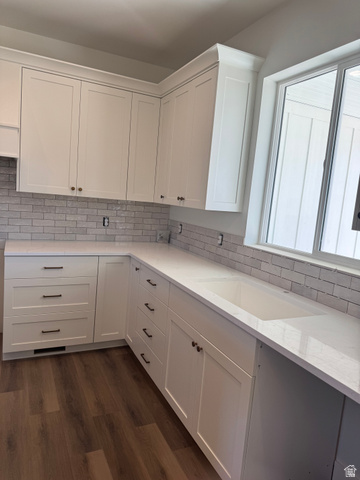 389 West 2100 South Perry, UT 84302 - Photo 15 of 21 White shaker-style cabinetry with gold-tone hardware, subway tile backsplash, solid surface countertops, integrated sink, and wood-finish flooring