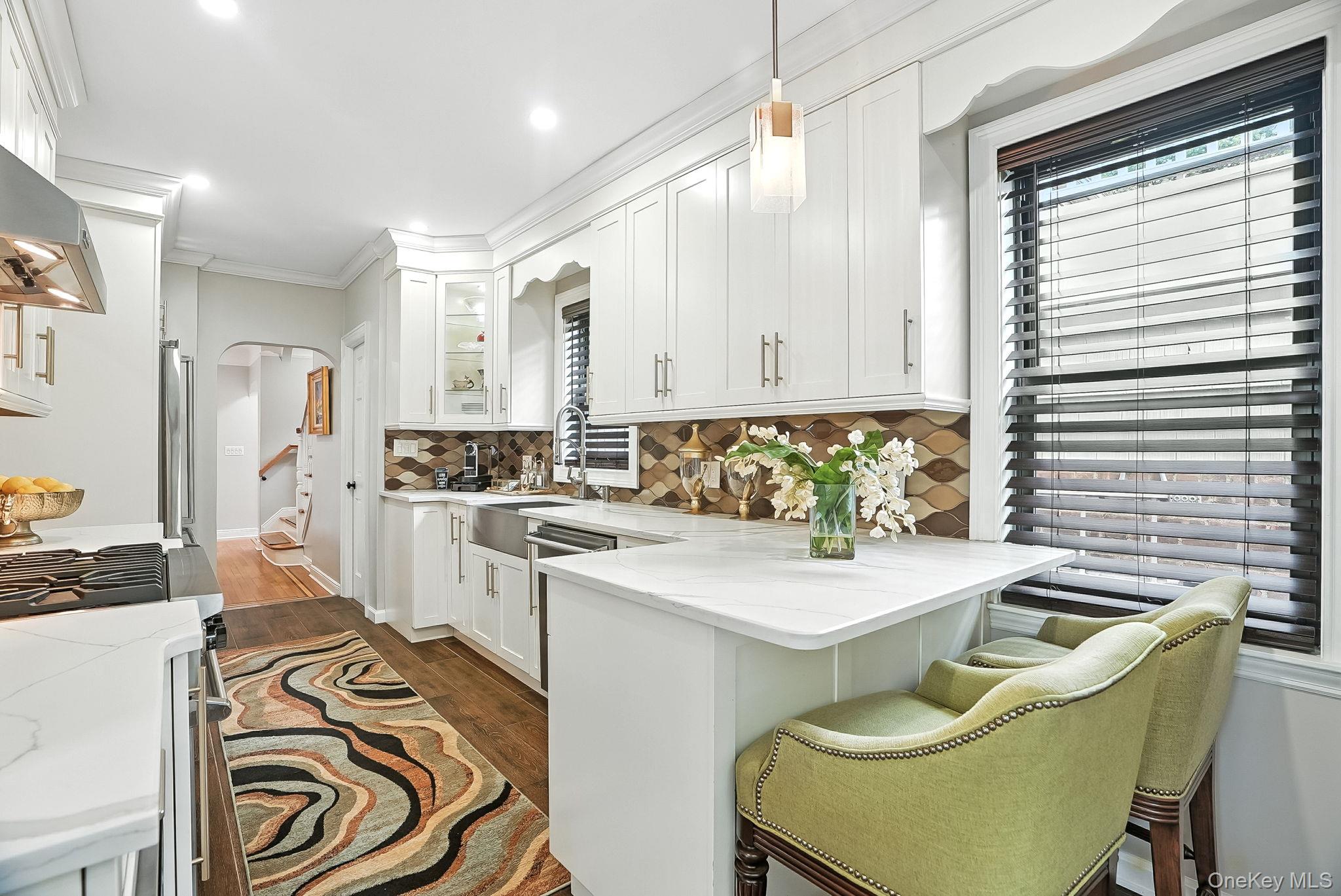 1260 Rhinelander Avenue Bronx, NY 10461 - Photo 15 of 50 Kitchen featuring arched walkways, ornamental molding, decorative backsplash, dark wood-style floors, and white cabinets