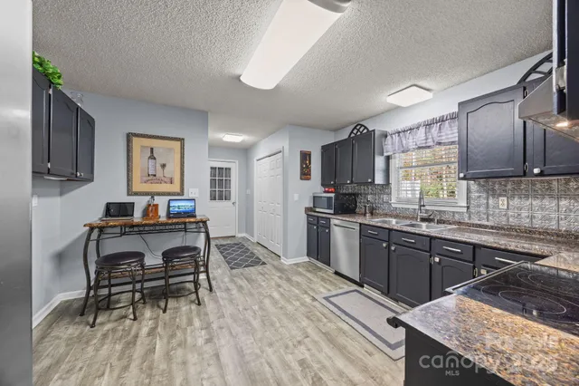 a kitchen with stainless steel appliances granite countertop a stove top oven a sink dishwasher a dining table and chairs with wooden floor