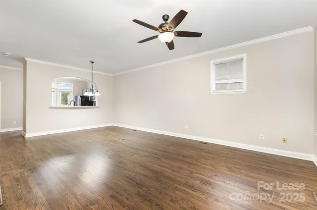 a view of an empty room with wooden floor and a ceiling fan