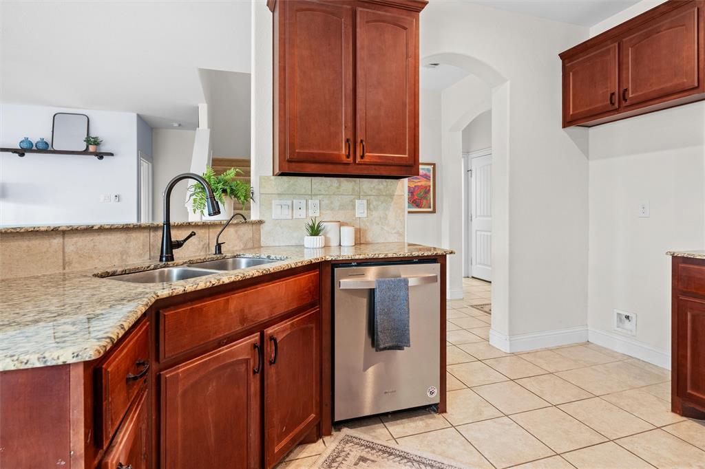 2322 Trace Ridge Drive Weatherford, TX 76087 - Photo 13 of 30 Kitchen featuring light stone countertops, stainless steel dishwasher, light tile patterned floors, arched walkways, and tasteful backsplash