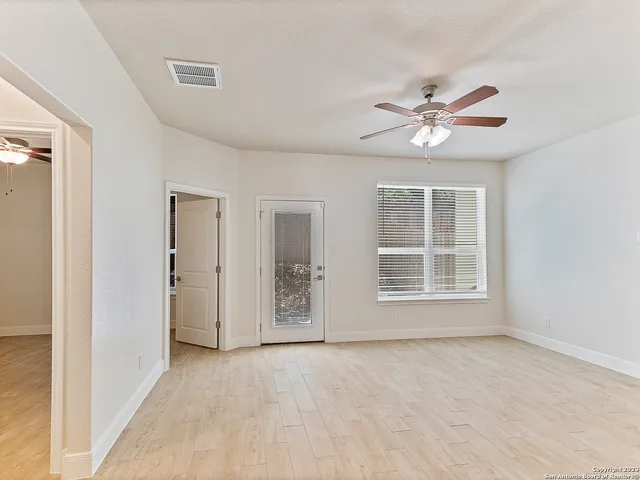 an empty room with chandelier fan and windows