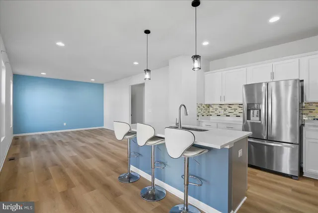 a kitchen with stainless steel appliances a refrigerator a sink dishwasher a dining table and chairs with wooden floor