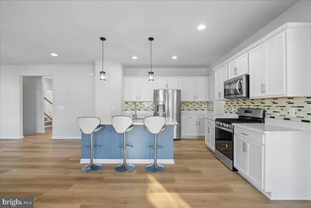 a kitchen with kitchen island granite countertop a stove a sink a refrigerator and white cabinets with wooden floor