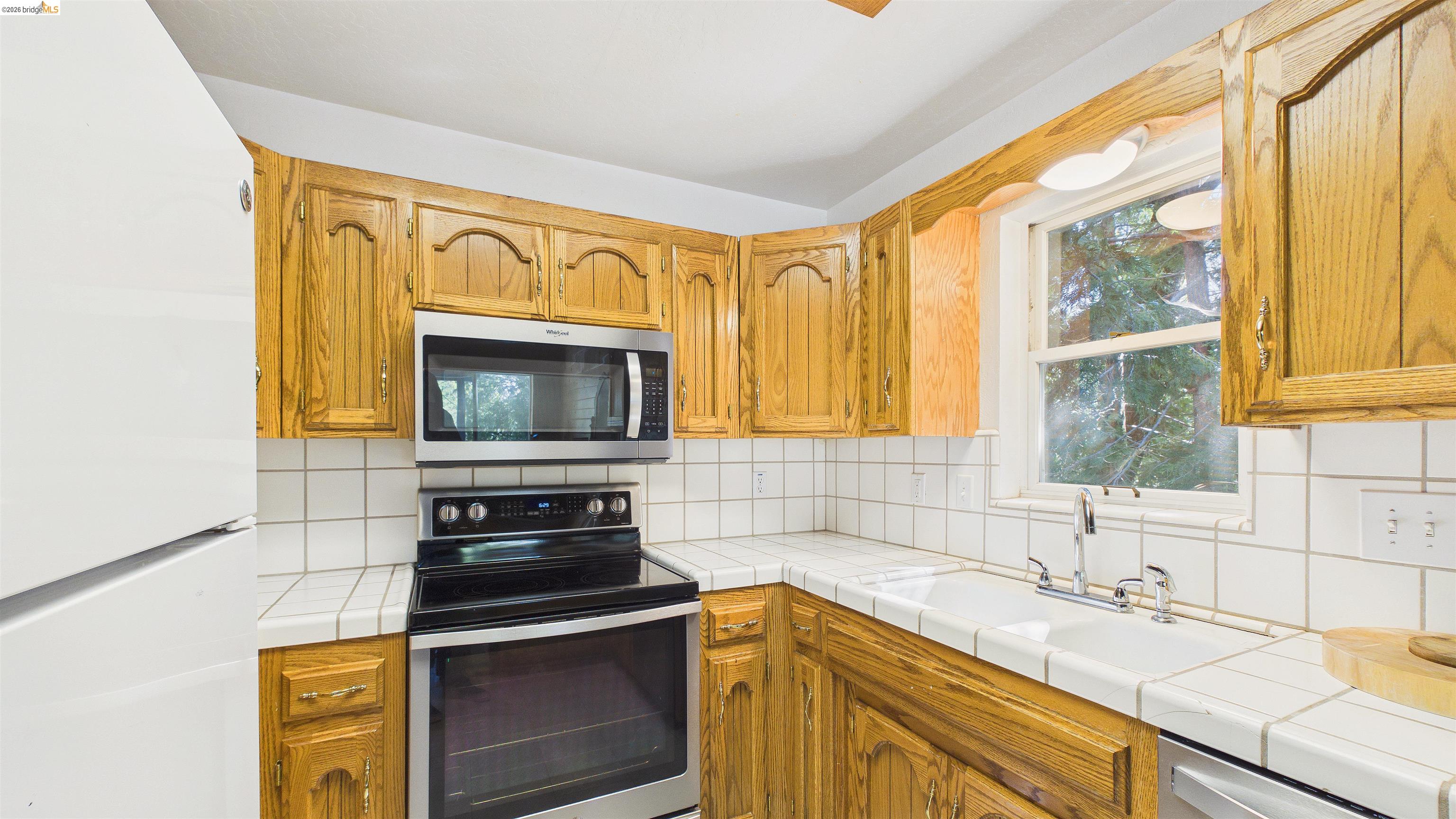 26570 Crystal Road Long Barn, CA 95335 - Photo 13 of 39 Kitchen featuring wood cabinetry, white tile countertops, white tile backsplash, stainless steel microwave, and a stainless steel electric range
