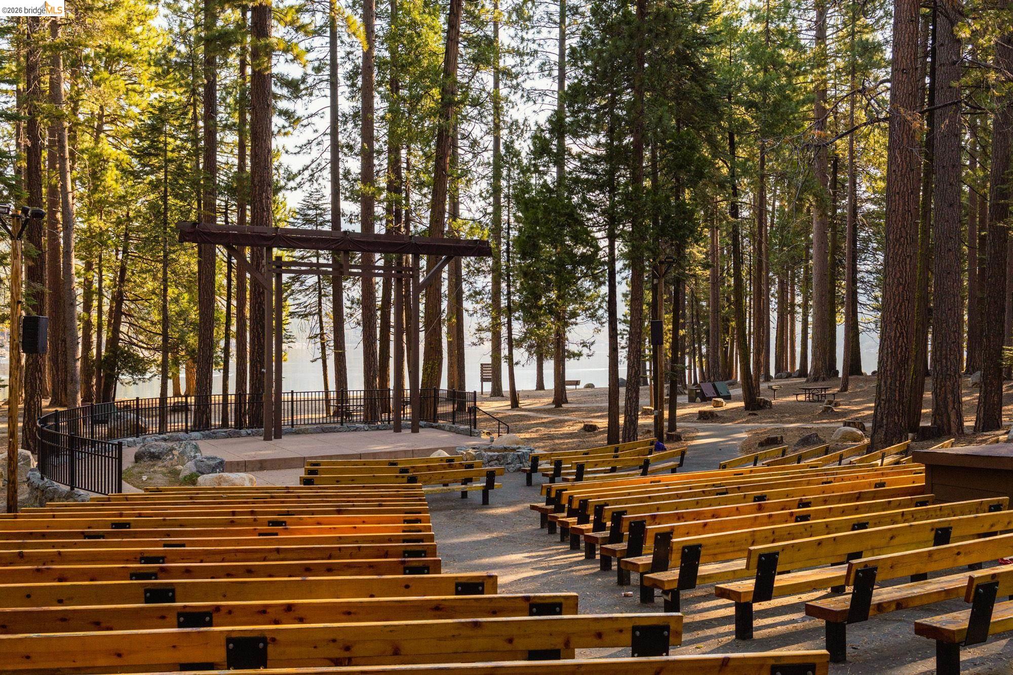 26570 Crystal Road Long Barn, CA 95335 - Photo 34 of 39 Outdoor amphitheater featuring rows of wood seating, a wood stage structure, a black metal fence, and a backdrop of mature pine trees