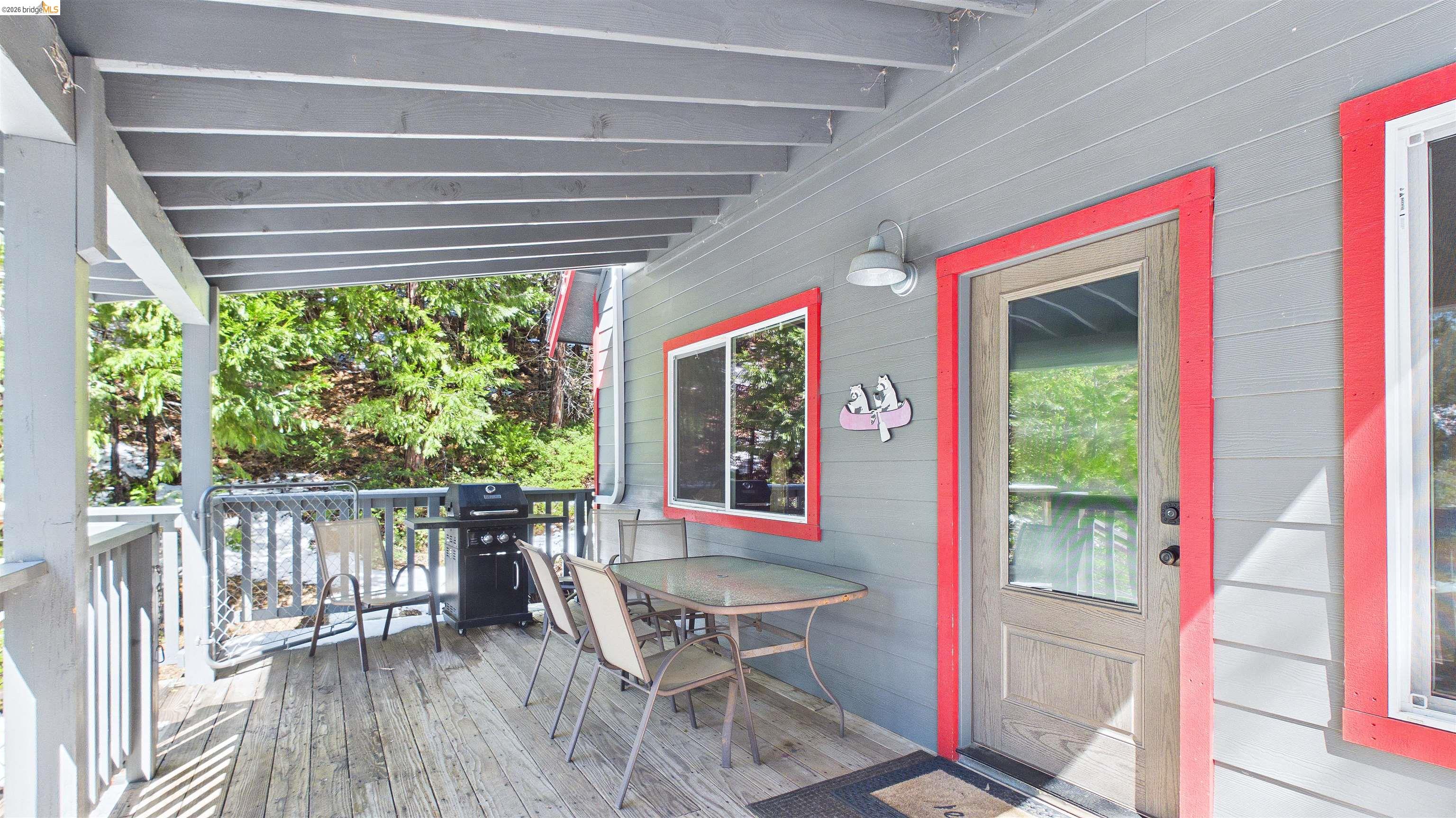 26570 Crystal Road Long Barn, CA 95335 - Photo 7 of 39 Covered outdoor deck with wood flooring and railing, featuring a panel-in-frame entry door with a glass insert, and exterior siding with contrasting trim