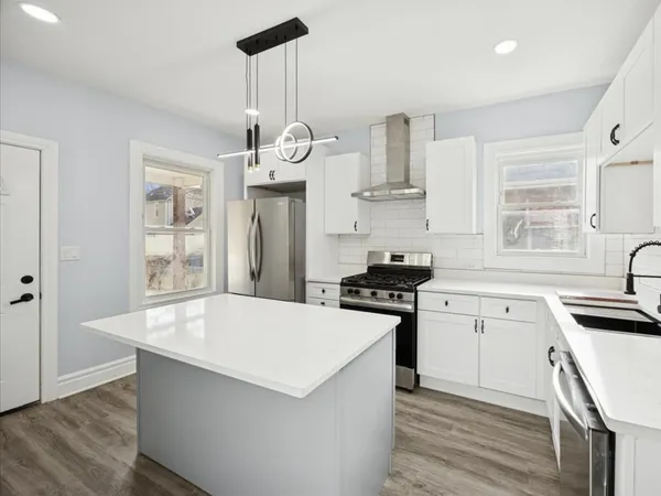 a kitchen with stainless steel appliances a stove a sink dishwasher a refrigerator and white cabinets with wooden floor