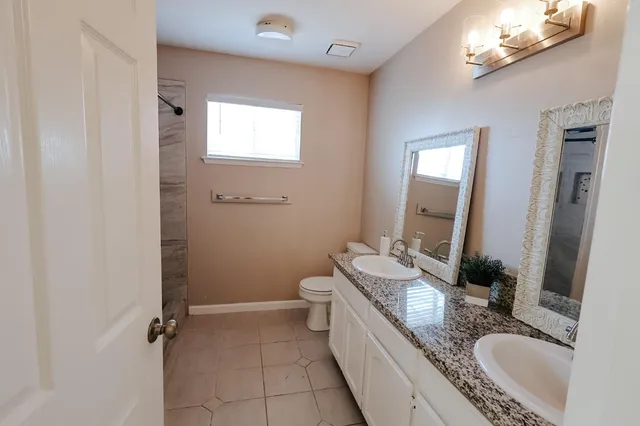 a bathroom with a granite countertop double vanity sink a mirror and a shower