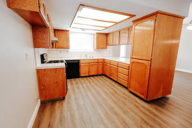 a kitchen with stainless steel appliances granite countertop a refrigerator a sink dishwasher a stove and white countertops with wooden floor