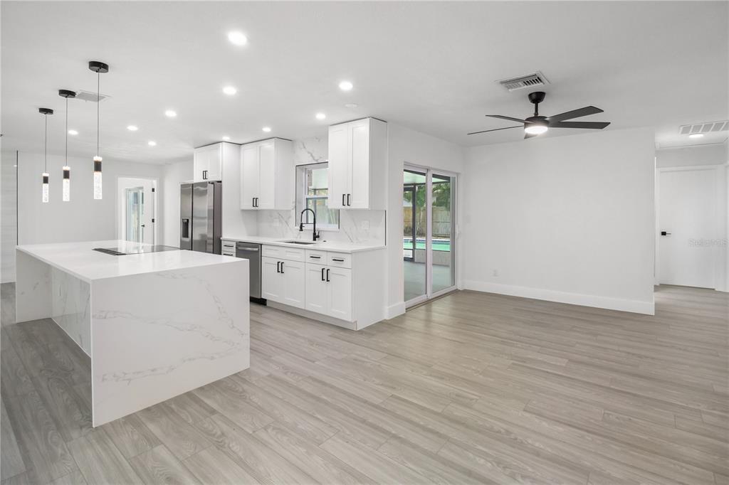 11492 93rd Street Largo, FL 33773 - Photo 17 of 37 a large white kitchen with kitchen island a stove a sink a refrigerator and white cabinets with wooden floor