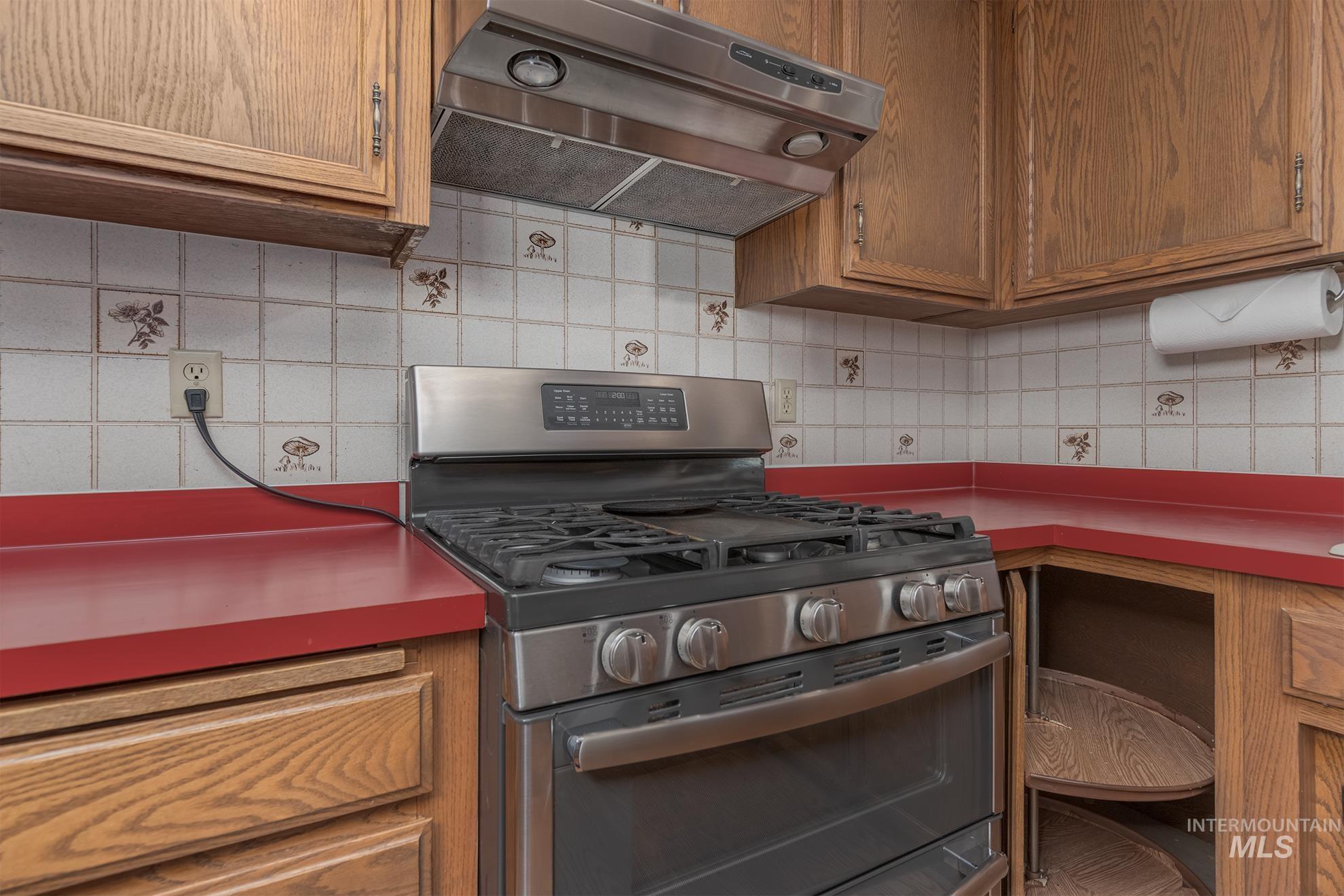 340 Pioneer Road Weiser, ID 83672 - Photo 19 of 44 Stainless steel range with a coordinating range hood, wood cabinetry, red countertops, and tiled backsplash