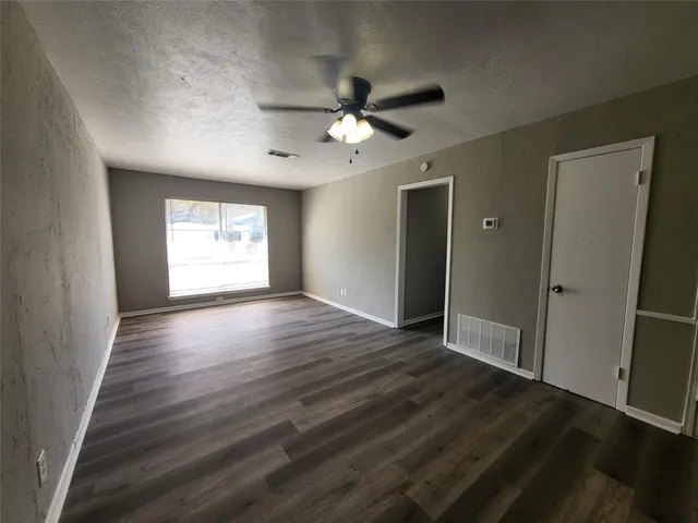 an empty room with wooden floor fan and windows