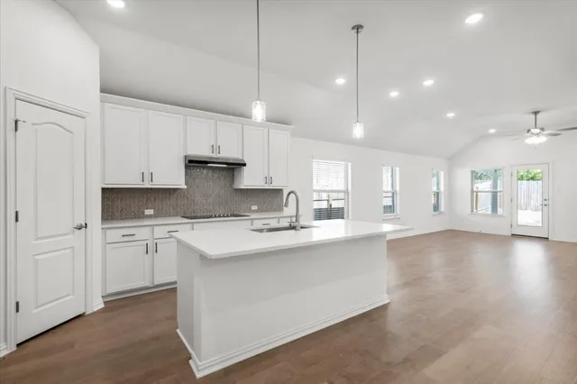 a large kitchen with granite countertop a stove a sink a refrigerator and white cabinets with wooden floor