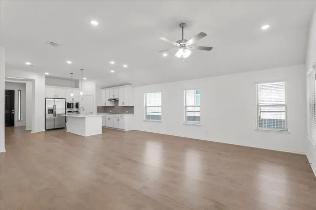 a view of an empty room with kitchen and window