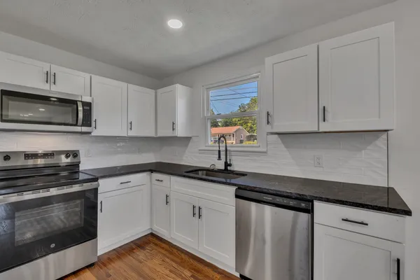 a kitchen with granite countertop white cabinets appliances and a sink
